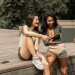 cheerful young multiethnic women sharing laptop and laughing in park